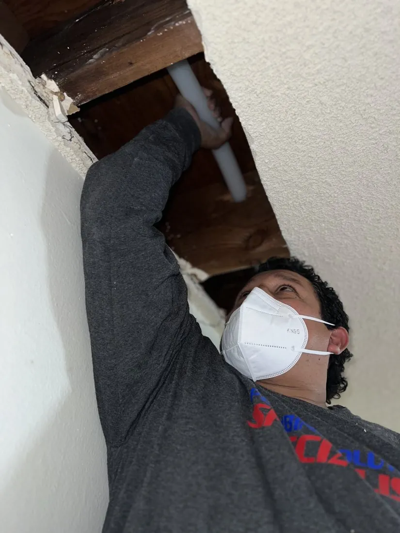 Technician accessing plumbing through a ceiling opening