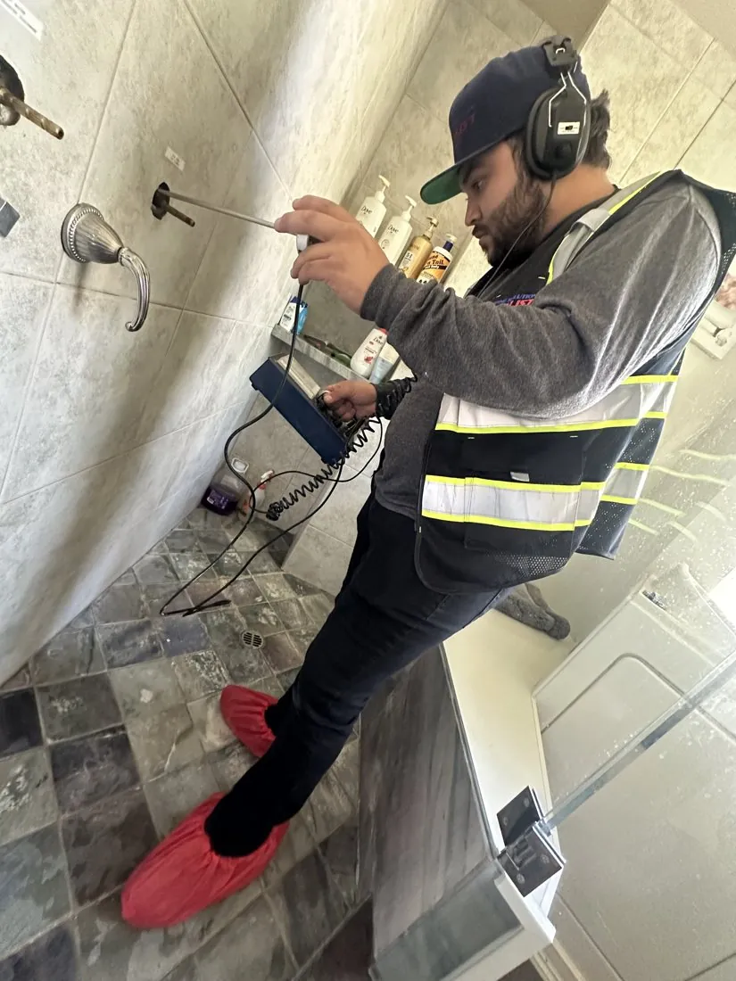 Technician inspecting plumbing at a wall opening