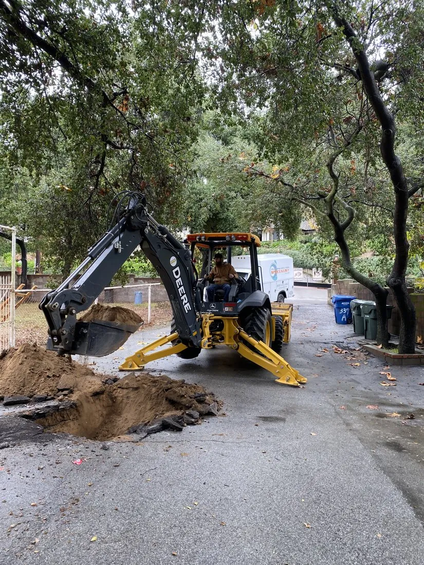 Backhoe excavating paved ground at a plumbing work area