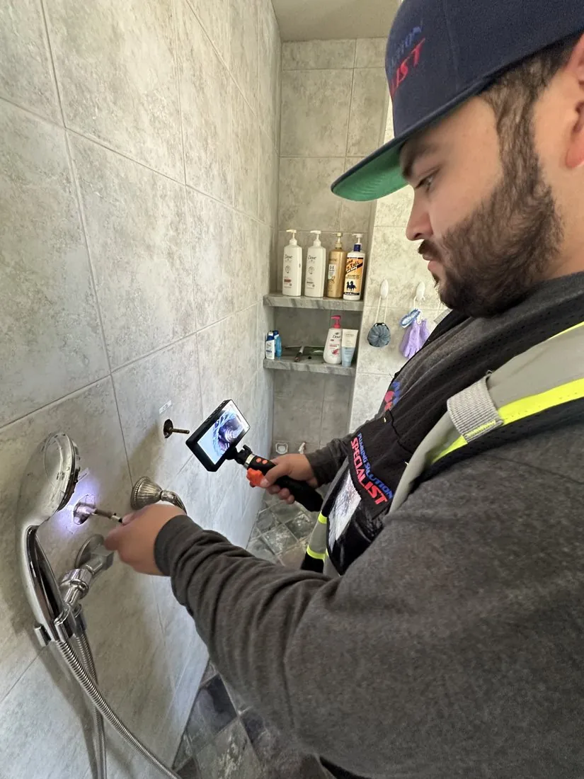 Technician using an inspection camera at a shower wall opening